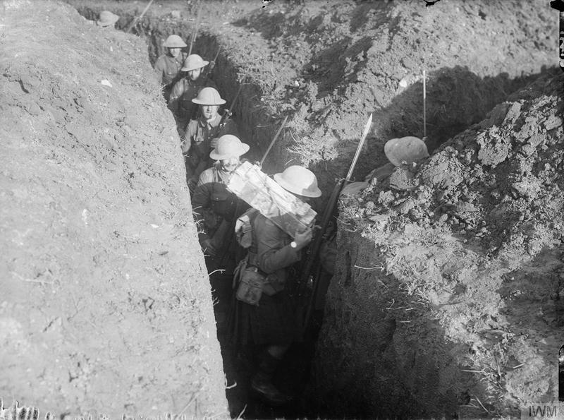 Cameron Highlanders, walk through in a narrow communication trench, situated between Pozieres and Le Sars, in the region of the Battle of the Somme, October 1916. One Highlander carries a box of grenades over his shoulder. Imperial War Museum image Q1497