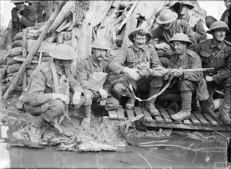 A group of guards, including Coldstream Guards and Irish Guards, crouching outside a captured German dugout, examining a muddy German rifle, near Langemarck (Langemark-Poelkpelle), 12 October 1917. Imperial War Museum image Q3011
