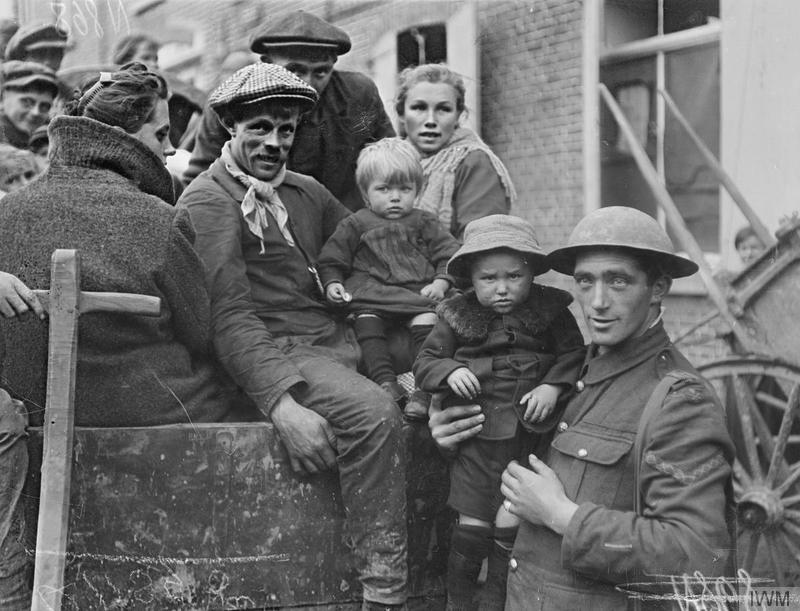 Belgian refugee family in a British horse-drawn wagon. Courtrai, 18 October 1918. British soldier holding one of their children. Imperial War Museum image Q11395. The soldier has a wound stripe.